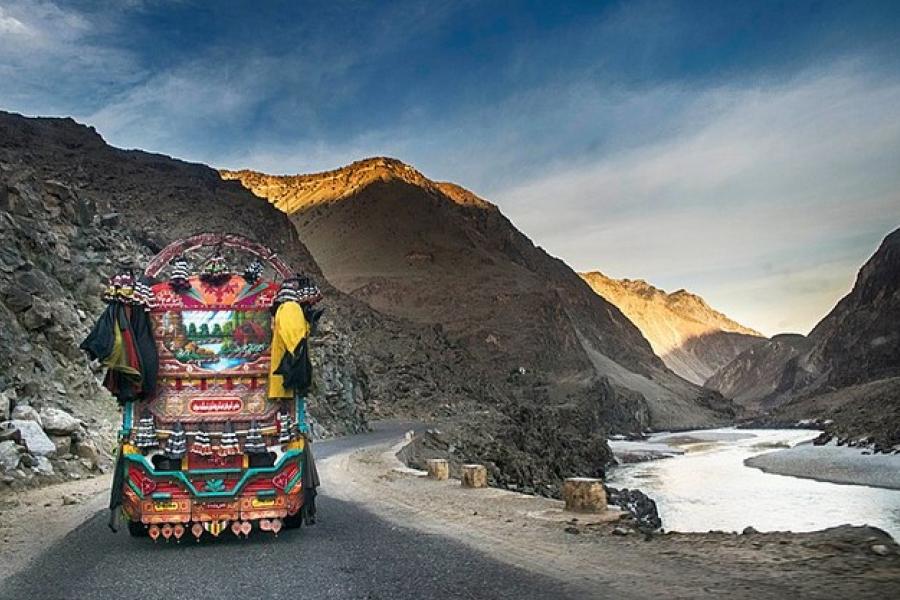 Karakoram Highway - A colourfully decorated bus on a road beside a river.